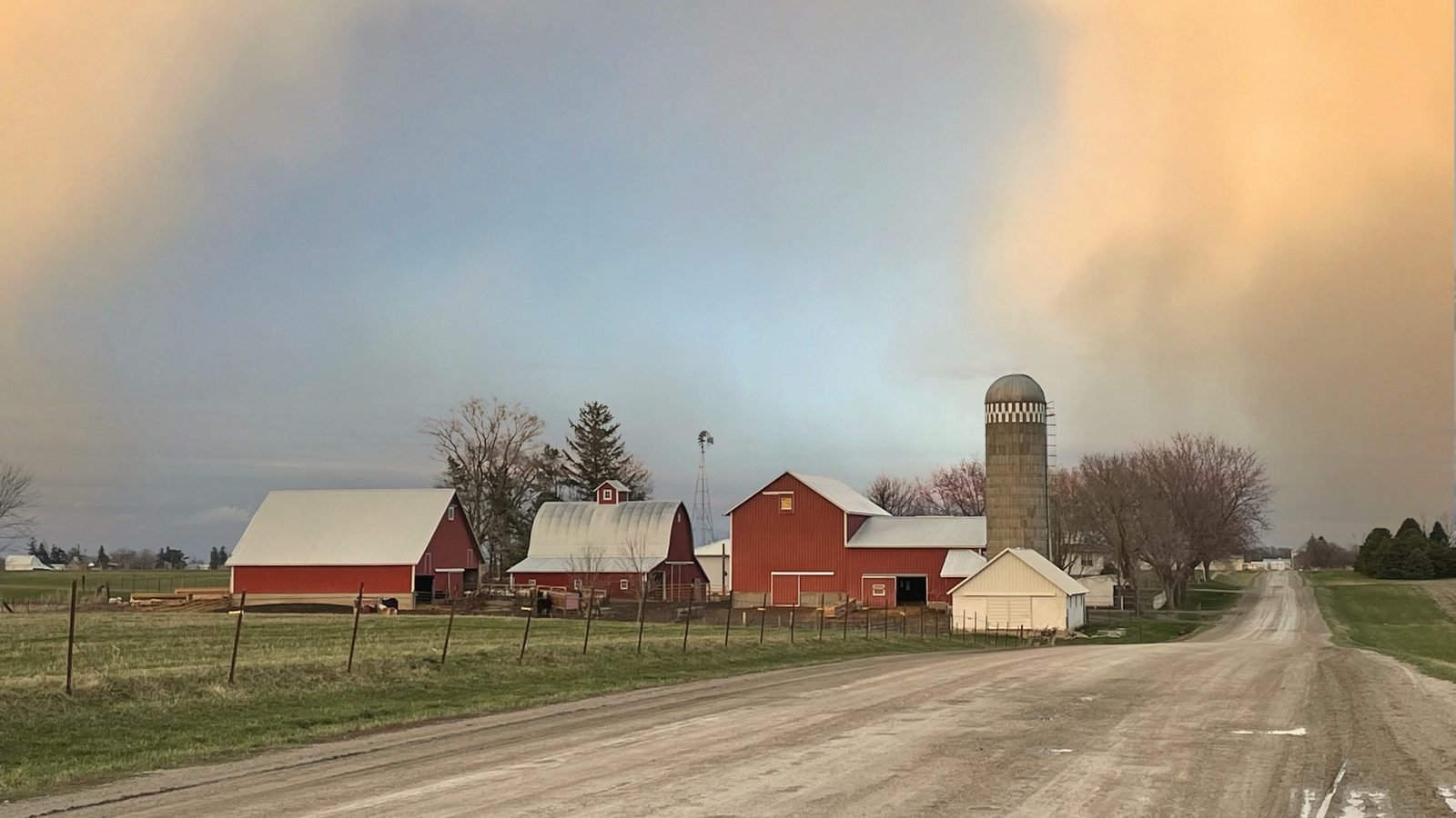 A gravel road leading past red barns and a concrete silo