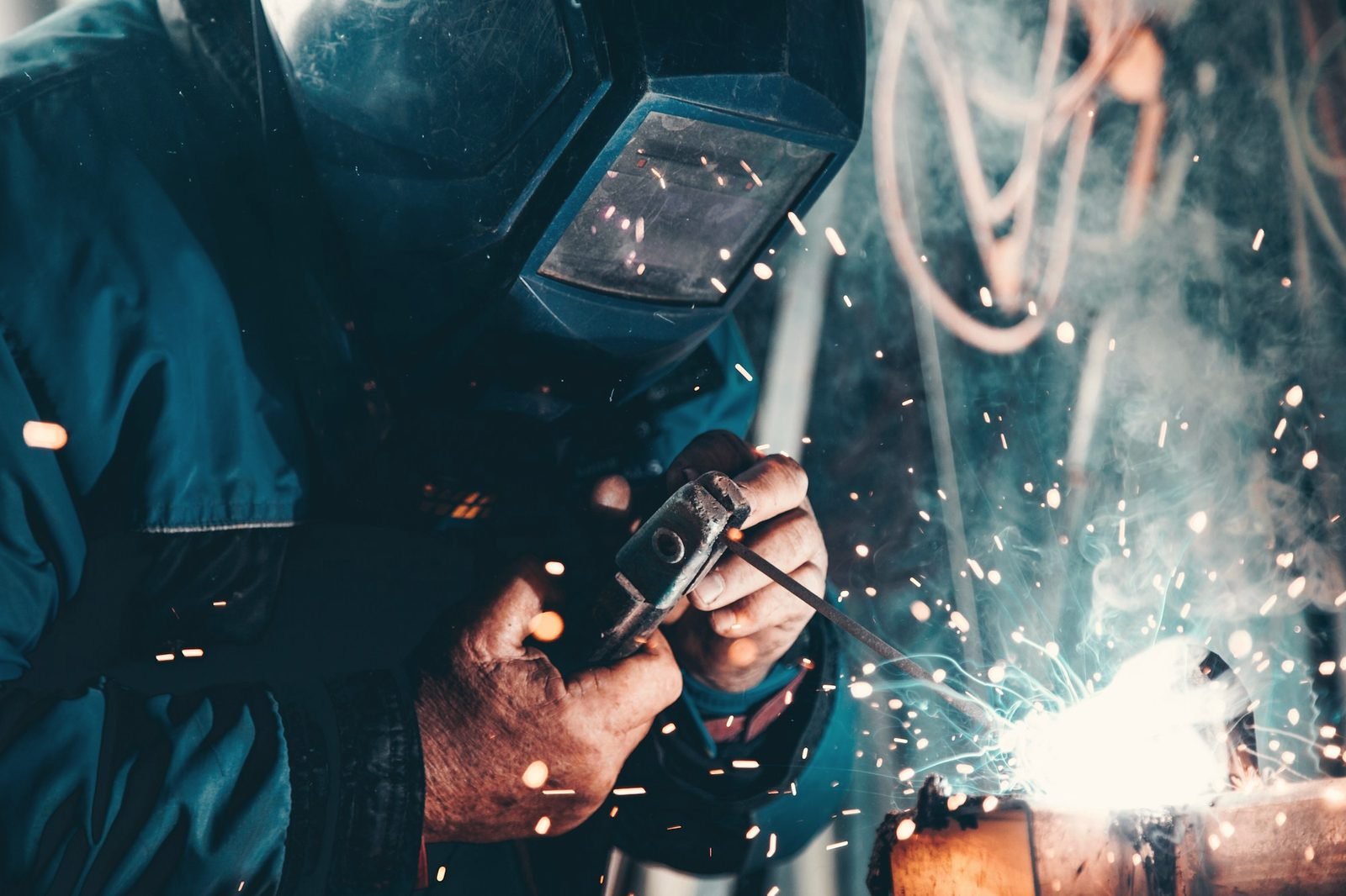 Gloved hands welding with sparks under a welding helmet